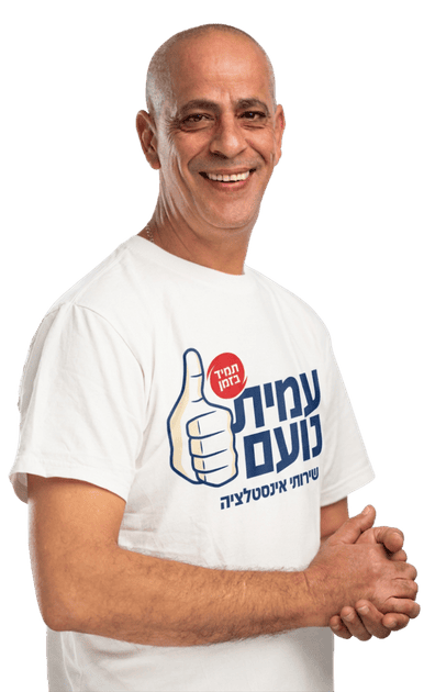 גבר קירח ומחייך, לבוש בחולצת טריקו לבנה עם כיתוב בעברית וגרפיקה של אגודל מורם, עומד על רקע לבן חלק, כשידיו משולבות זו בזו. | עמית נעם תמיד בזמן - אינסטלוטור בתל אביב